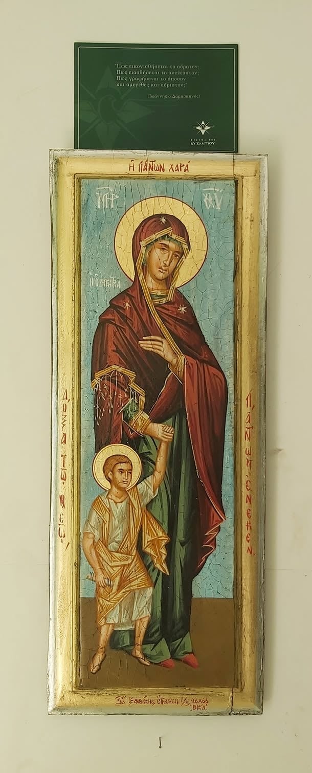 Orthodox icon depicting Virgin Mary in red robes holding Christ Child, with gold halos and Greek text, mounted in wooden frame
