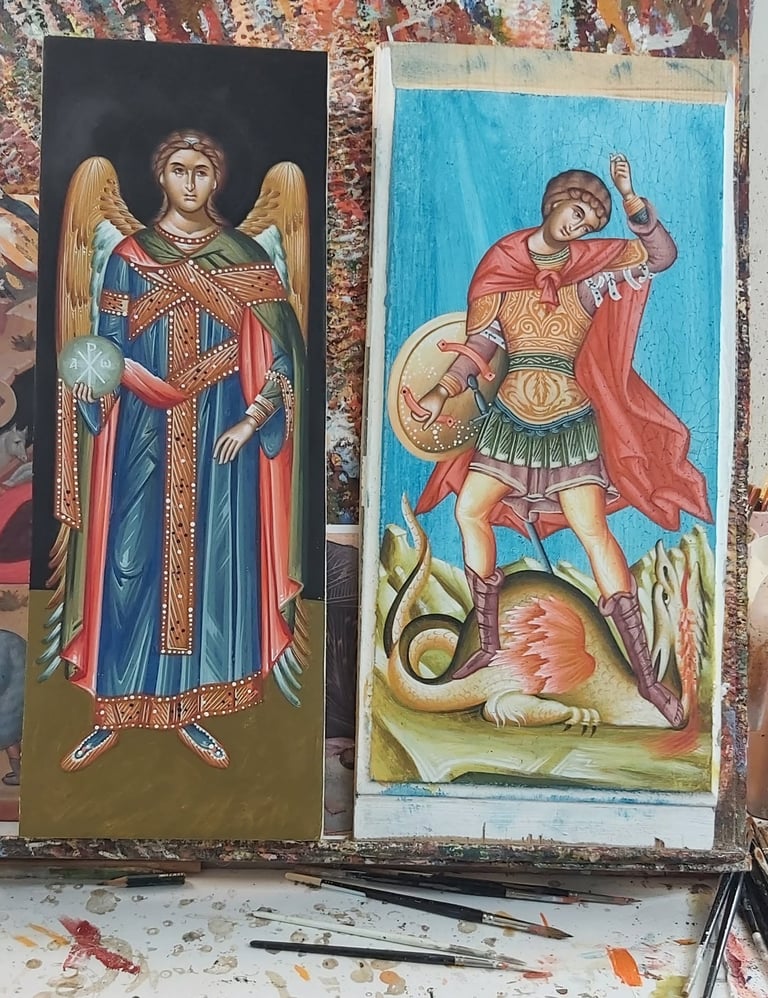 Two religious icon paintings displayed side by side: left shows an angel in ornate robes with wings and gold trim; right depicts Saint George slaying a dragon in traditional Byzantine style.