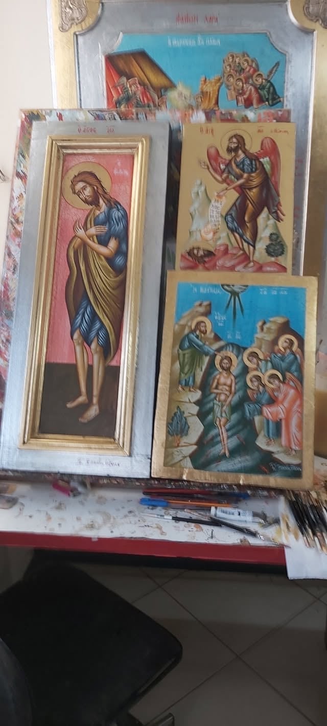 Collection of religious Orthodox iconography displayed on a white surface, including framed icons with gold borders depicting saints and biblical scenes