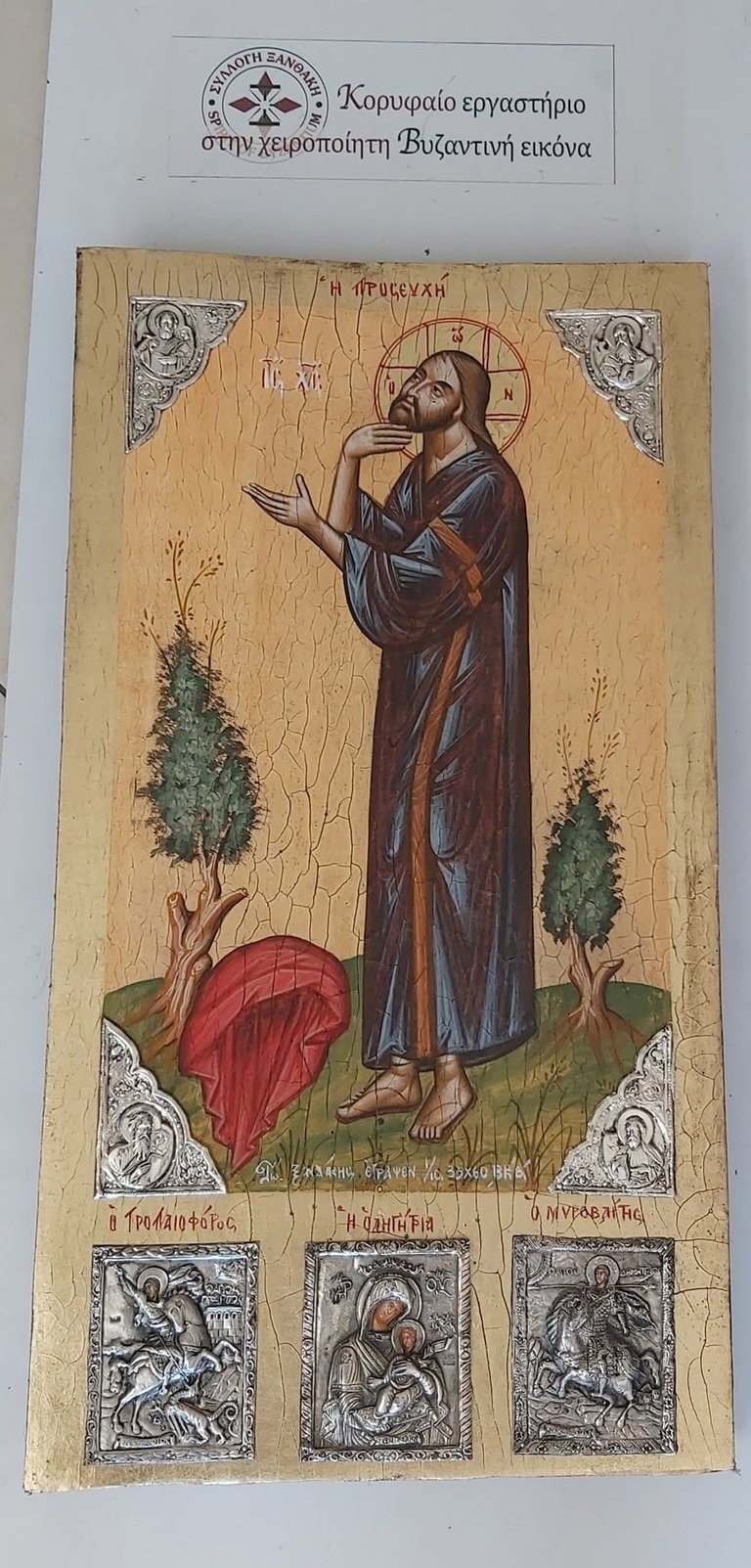 Byzantine religious icon depicting Saint John in prayer, wearing robes with ornamental corners and three smaller religious scenes at bottom