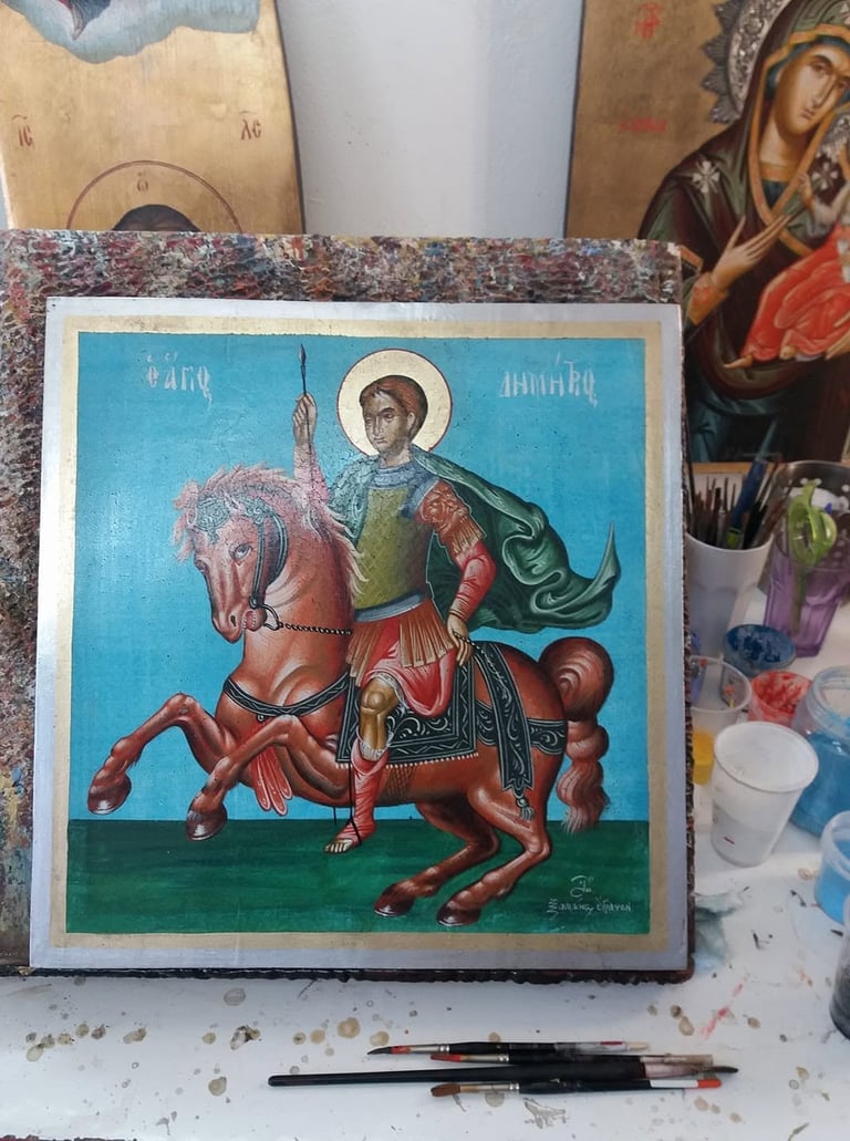Religious icon painting depicting a saint with halo on horseback against a blue background, displayed among art supplies and religious items