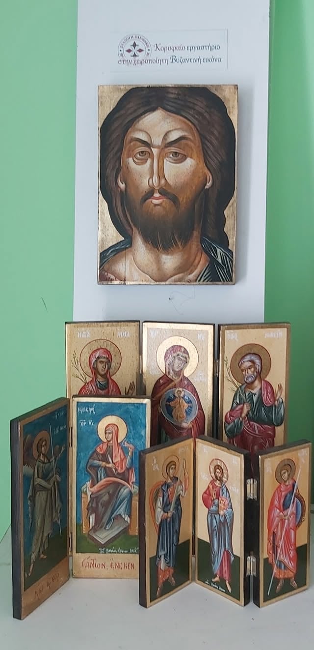 Orthodox religious icon collection displayed on white wall, featuring a large Christ Pantocrator icon at top and a multi-paneled wooden iconostasis below showing various saints
