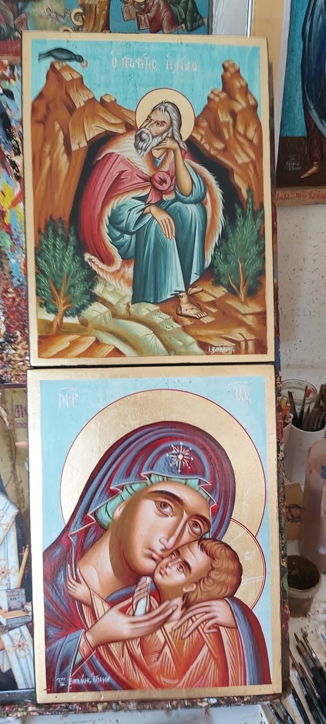 Two Orthodox Christian religious icons on display, showing a saint with halo in mountain landscape above and Madonna with child below