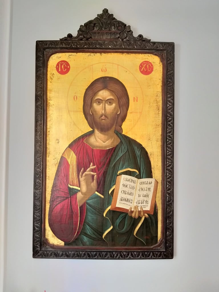 Religious icon of Jesus Christ wearing red and green robes, holding an open book, set in an ornate dark metal frame against a white wall