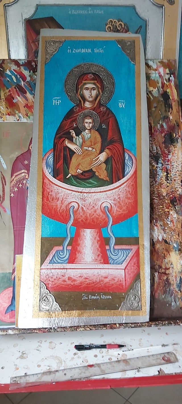 Orthodox religious icon depicting Virgin Mary holding Christ child, with ornate red altar base and blue background, surrounded by craftwork materials.