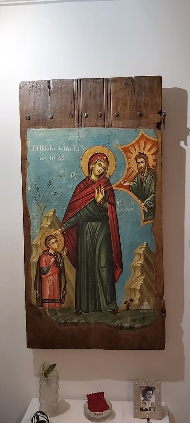 Ancient Orthodox Christian icon on wooden panel featuring robed religious figures with halos against a blue background, displayed on a white gallery wall