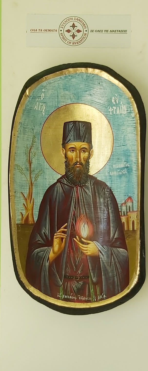 Orthodox Christian icon of a bearded saint with a halo, wearing dark monastic robes and a tall head covering, holding a flame and a scroll, with a desert landscape background