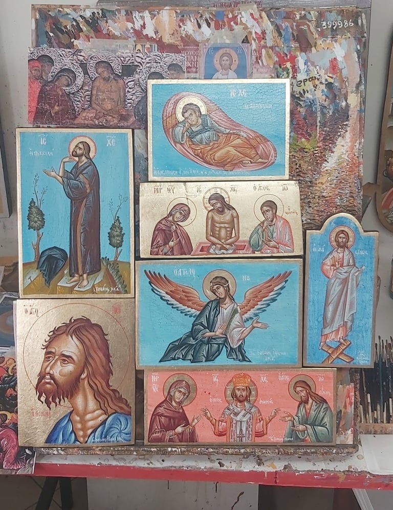 Collection of Byzantine-style religious icons displayed on a work table, featuring depictions of saints, angels, and religious figures in traditional Orthodox iconographic style