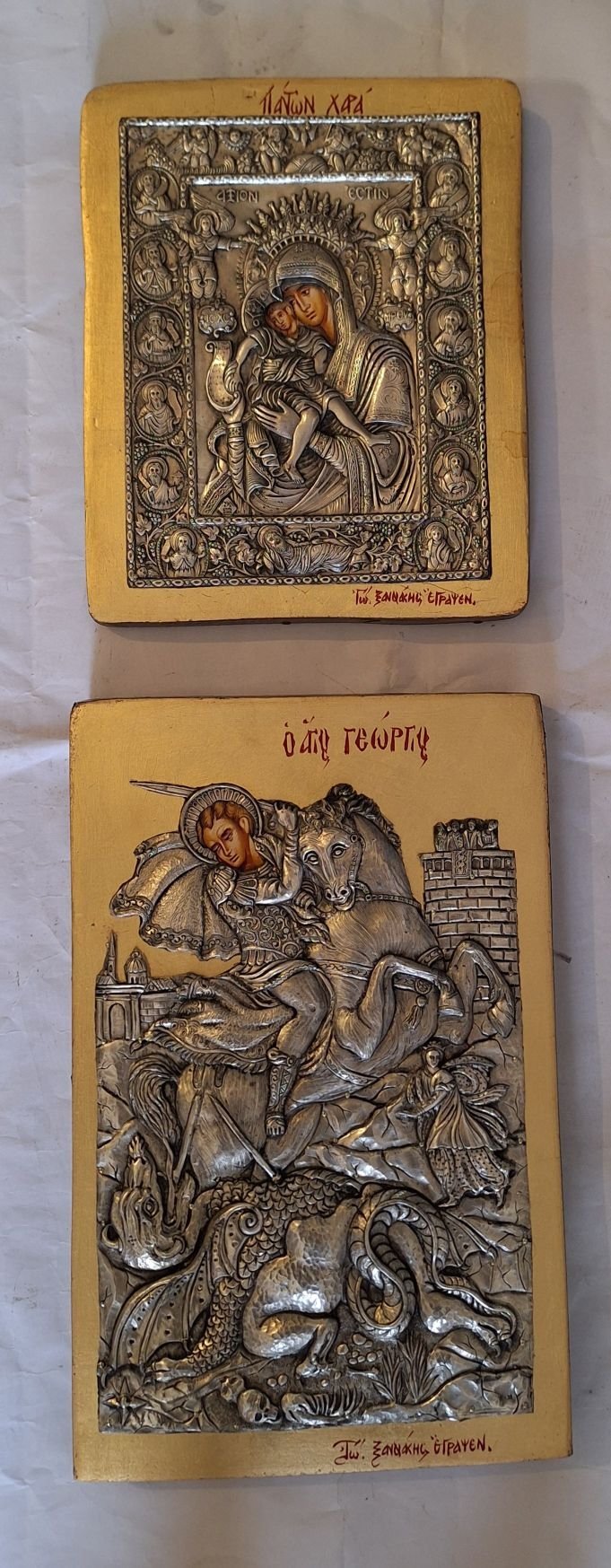 Two ornate wooden religious icon plaques with metal relief imagery depicting Orthodox Christian saints on yellow wood backgrounds