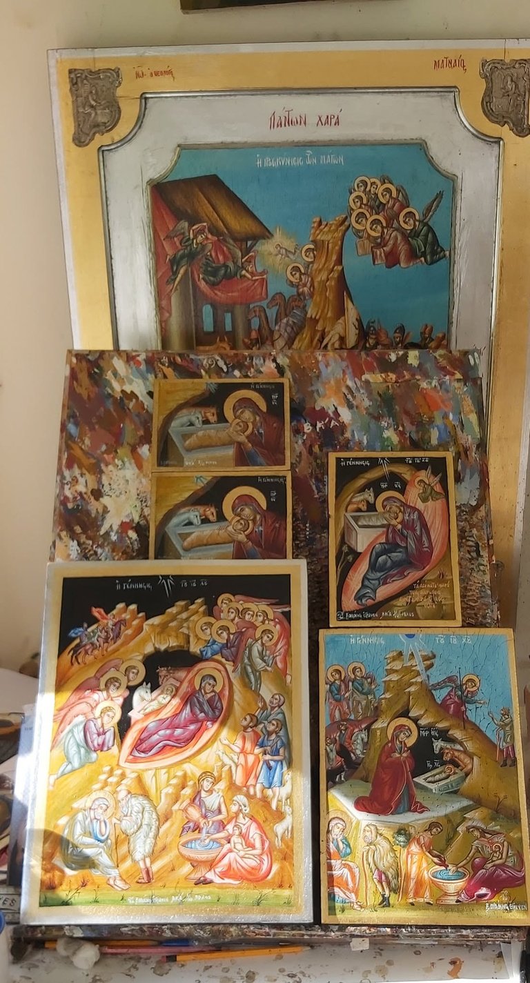 Collection of Orthodox Christian religious icons and artwork displayed on a wooden panel, featuring nativity and nativity-related scenes with gold accents