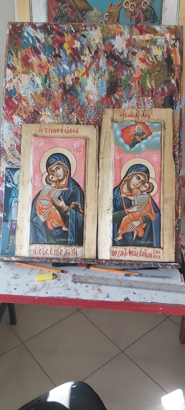 Two religious iconographic paintings on wooden panels displayed on a red table with a colorful abstract artwork above them