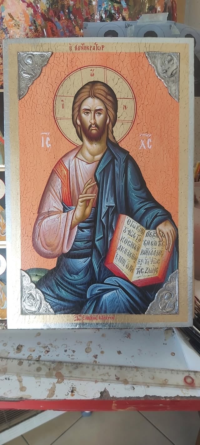 Orthodox religious icon depicting Jesus Christ in traditional robes with halo, holding a jeweled gospel book, painted on wooden panel with ornate silver corners.