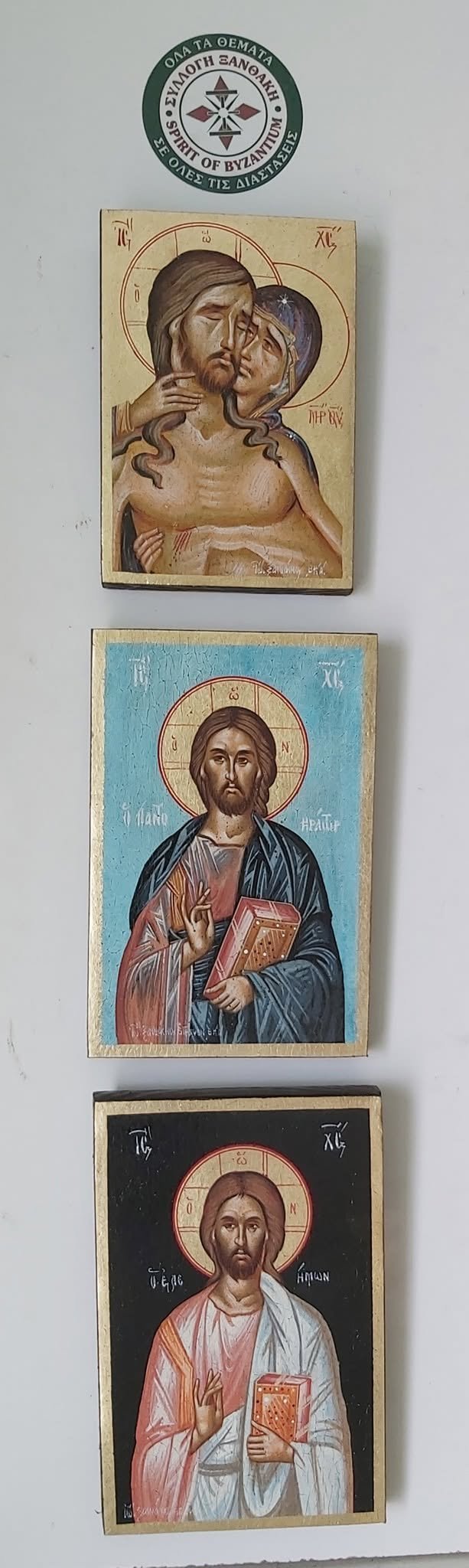 Three Orthodox Christian icon panels displayed vertically with a green monastery seal at top. Icons depict religious figures with halos and Byzantine artistic style on wooden panels with cream and colored backgrounds.