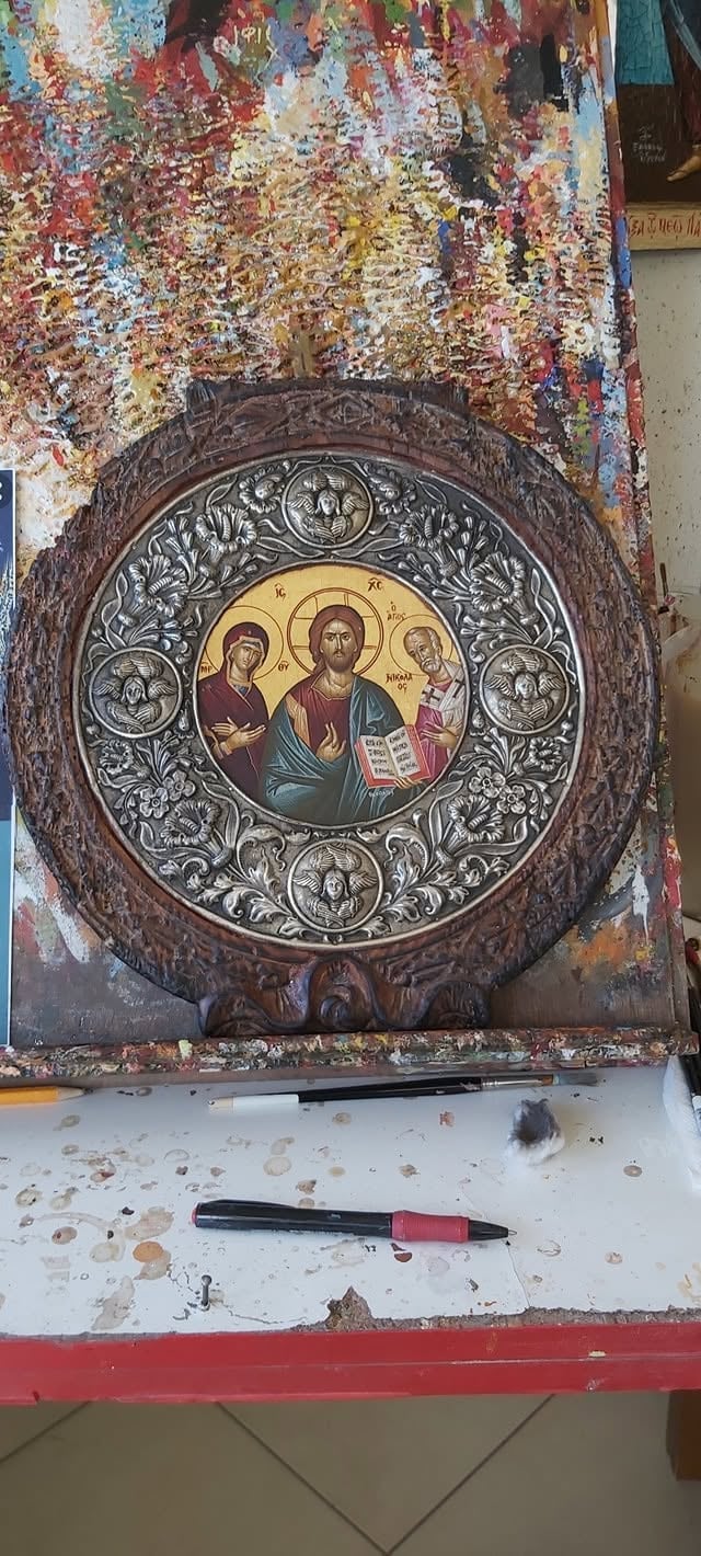 Ornate religious icon in circular wooden frame showing Christ with saints, displayed on weathered wall with colorful paint drippings