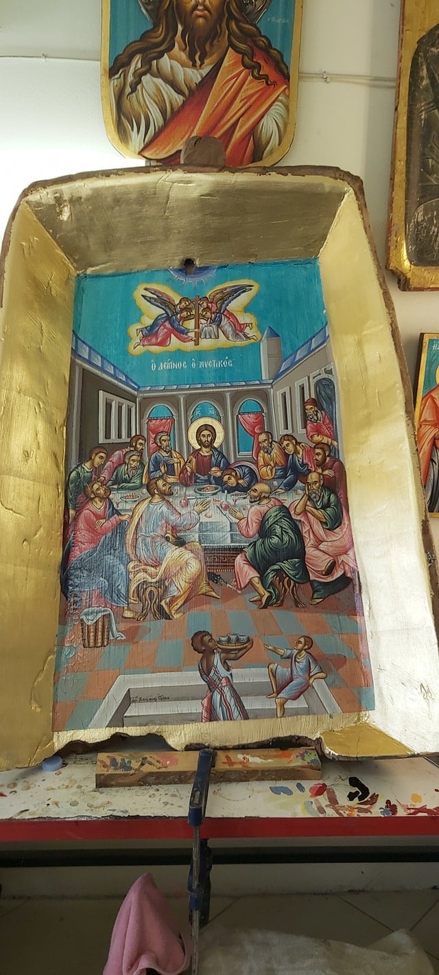 Orthodox wooden icon box with religious scenes depicting a feast gathering and angels at top, mounted on wall with gold frame