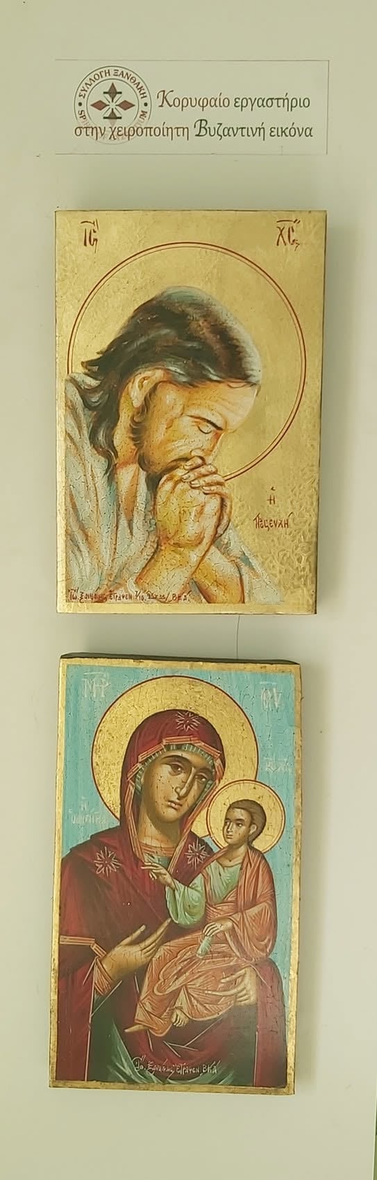 Two Byzantine religious icons displayed on a beige wall with Greek text header. Top icon shows a bearded saint with halo in contemplative pose. Bottom icon depicts Mary holding the Christ Child, both with golden halos against turquoise background.