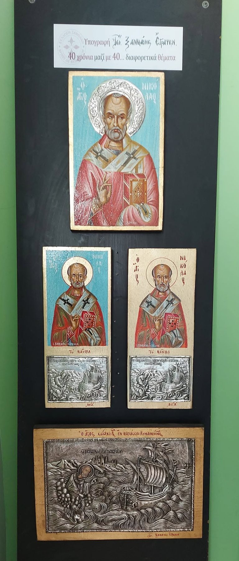 Museum display of Orthodox religious icons showing Saint Nicholas in various artistic styles and periods, including colored and engraved representations on dark background