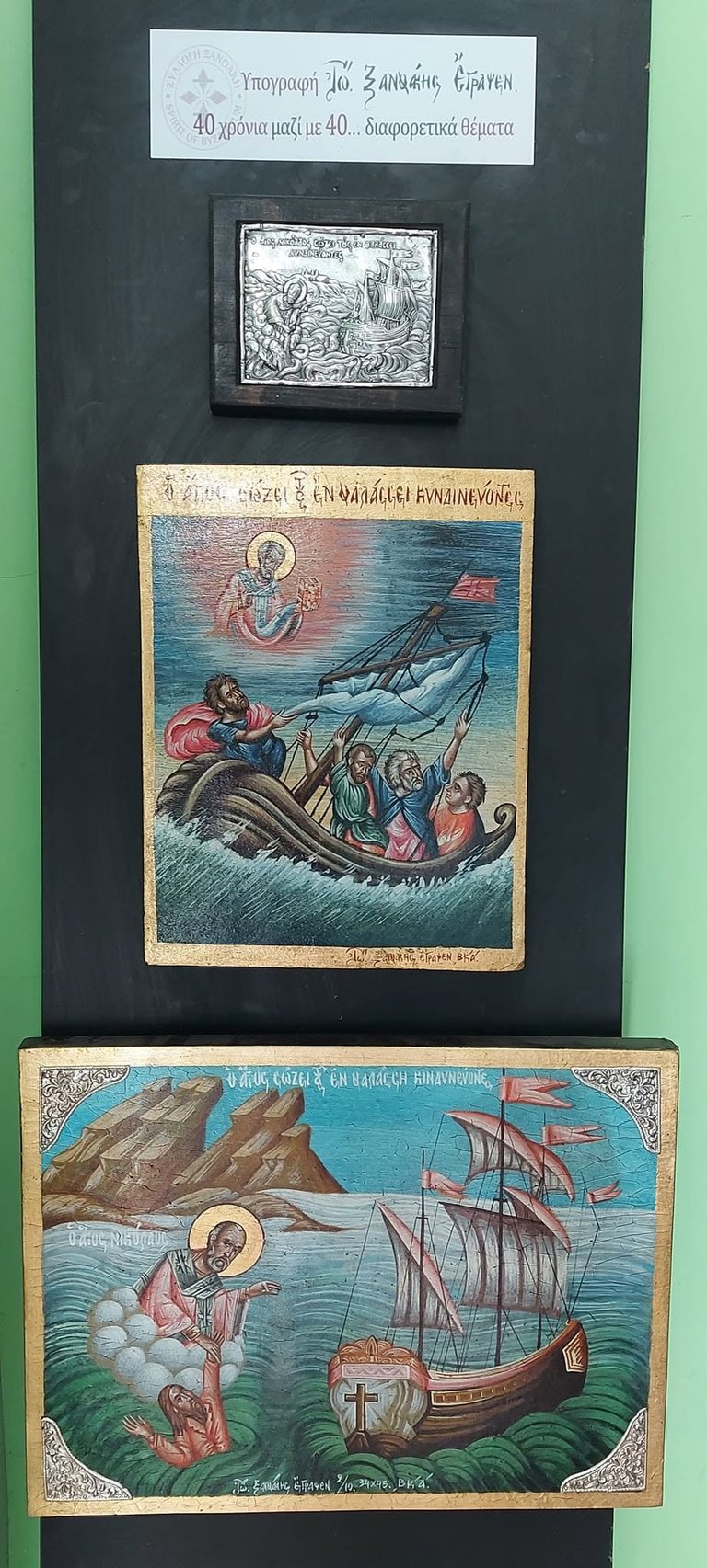 Museum display of three religious icons showing biblical maritime scenes with Greek text labels against a dark background