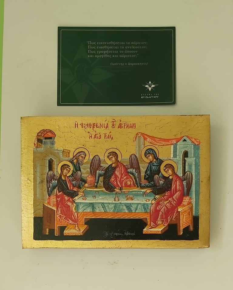 Two religious plaques displayed on a beige wall: a green plaque with Greek text and a golden Byzantine-style icon depicting angels gathered around a table.
