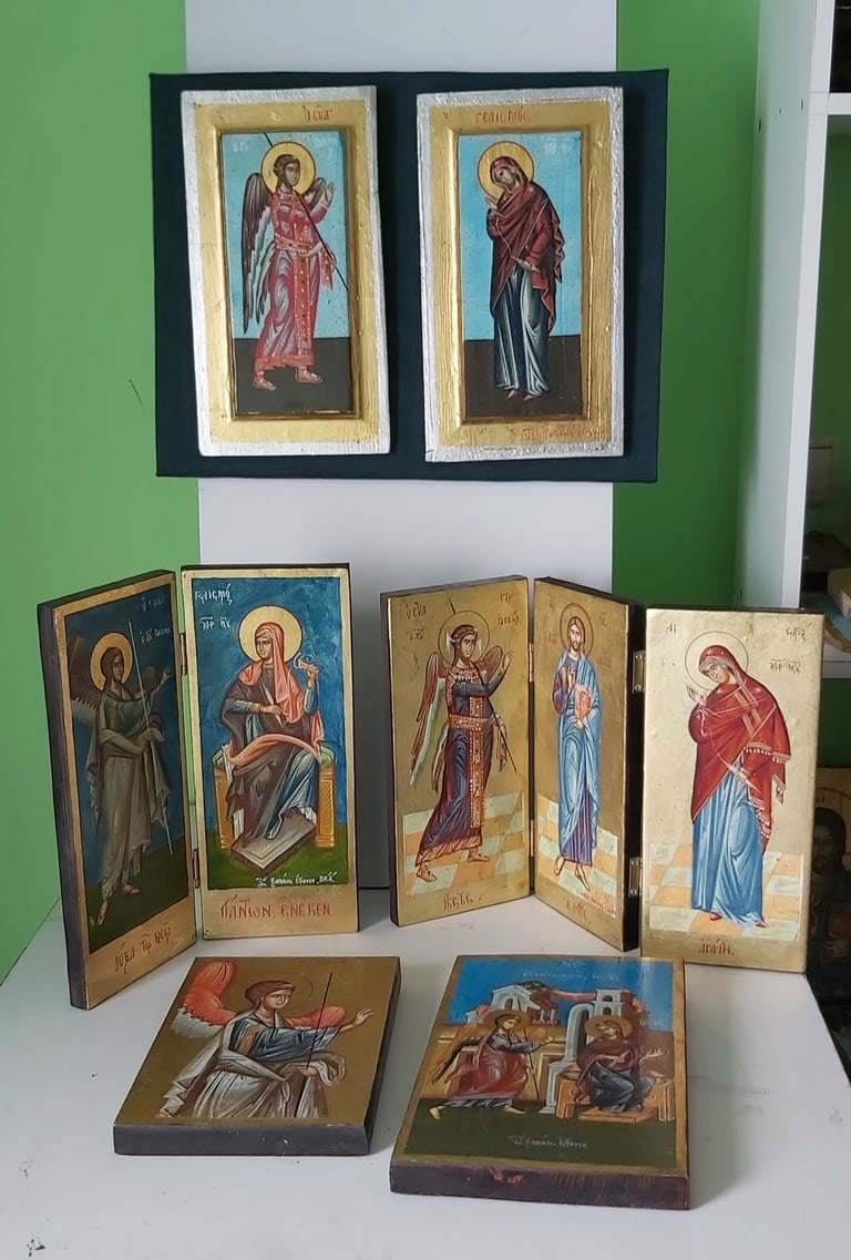 Collection of religious Orthodox icons displayed on a white surface against a green wall, including framed pairs and folding diptychs.