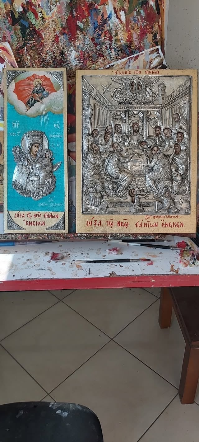 Two Orthodox religious icons and engravings displayed on a paint-splattered table with brushes below